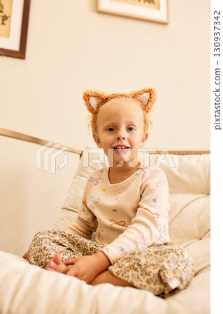 Child with cat ears headband smiling indoors on a cozy sofa 130937342