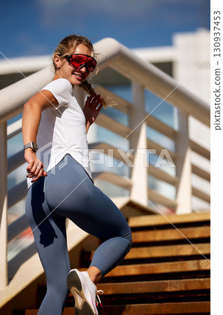 Young woman running up stairs outdoors in bright sunlight wearing athletic wear 130937453