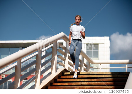 Young woman jogging down stairs outdoors on a sunny day Young woman jogging down stairs outdoors on a sunny day 130937455