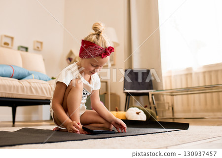 Young girl sitting on mat and exploring tablet in cozy living room 130937457