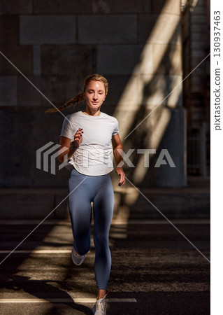 Young woman running outdoors in an urban setting with dramatic sunlight 130937463