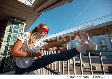 Active woman stretches outdoors during fitness workout on sunny urban morning Active woman stretches outdoors during fitness workout on sunny urban morning 130937685