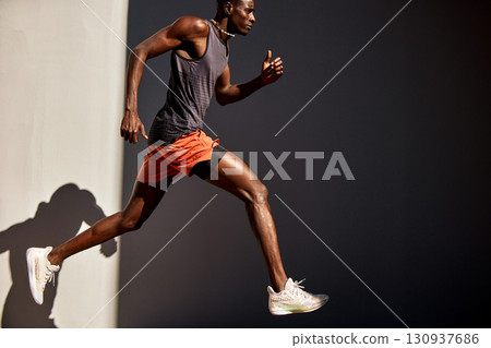 Athletic male runner in action wearing sportswear against dramatic lighting Athletic male runner in action wearing sportswear against dramatic lighting 130937686