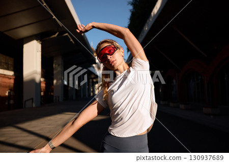 Athletic woman stretching outdoors wearing sunglasses during morning workout 130937689