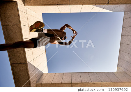 Dynamic low-angle shot of a sporty man leaping in urban architecture Dynamic low-angle shot of a sporty man leaping in urban architecture 130937692
