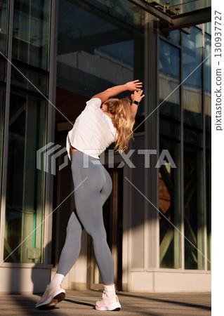 Active woman stretching outdoors in the warm sunlight by modern architecture Active woman stretching outdoors in the warm sunlight by modern architecture 130937727
