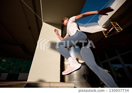 Athletic woman running outdoors near modern architecture in bright sunlight Athletic woman running outdoors near modern architecture in bright sunlight 130937734
