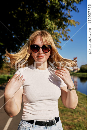 Woman Enjoying a Sunny Day Outdoors Wearing Sunglasses and Casual Attire 130937736