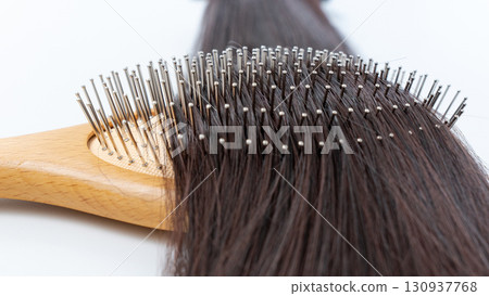 Wooden hairbrush with metal bristles resting on long, shiny, healthy hair, showcasing hair care and grooming essentials for vibrant locks 130937768