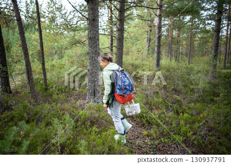 Traveler woman with backpack gathering mushrooms into basket while walking along forest edges Traveler woman with backpack gathering mushrooms into basket while walking along forest edges 130937791