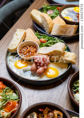 Traditional English breakfast with eggs, sausages, beans, bacon, and fresh bread on plate 130937878