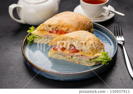 Ciabatta sandwich with cheese, ham and lettuce served with tea on a rustic black background 130937911