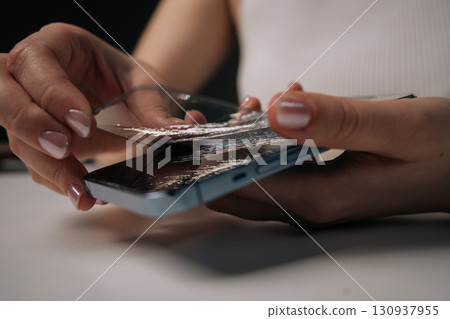 Hands of young unrecognizable woman removing broken tempered glass screen protector from mobile phone, showing importance of screen protection and potential damage it prevents. Hands of young unrecognizable woman removing broken tempered glass screen protector from mobile phone, showing importance of screen protection and potential damage it prevents. 130937955