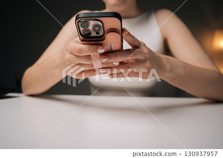 Cropped shot of woman holding sleek smartphone, featuring trendy protective case with hand strap, providing secure hold and contemporary style. Concept of modern technology and stylish accessories. 130937957