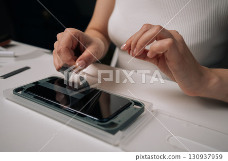 Close-up of woman installing screen protector on smartphone using specialized machine, ensuring perfect alignment and protection against scratches. Concept of mobile phone maintenance and service. 130937959