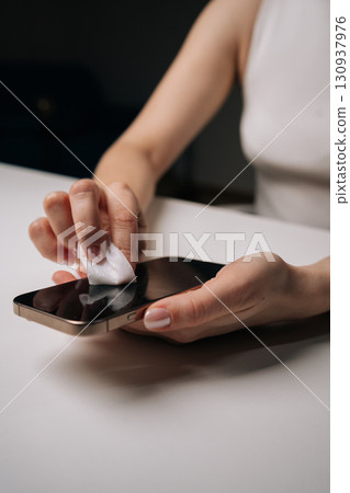 Woman carefully cleaning smartphone screen with disinfectant wipe, ensuring hygiene and removing fingerprints and smudges from glass surface, close-up. Concept of healthy lifestyle. 130937976