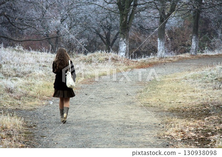 Young woman walks on a path through frosty trees 130938098