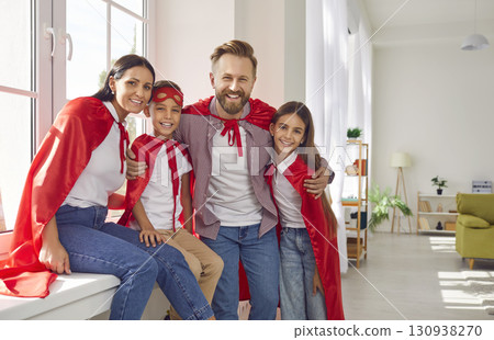 Happy family in superhero costumes sitting on the windowsill at home and looking at camera. 130938270