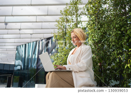 Young businesswoman using laptop outside office 130939053