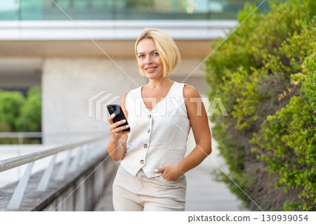 Smiling young blond businesswoman using smartphone 130939054