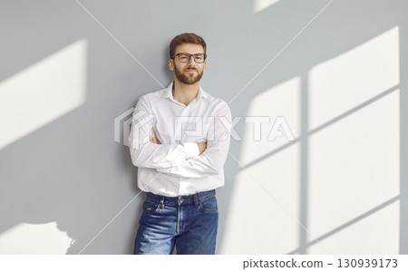Confident bearded man in eyeglasses posing with crossed arms at gray wall Confident bearded man in eyeglasses posing with crossed arms at gray wall 130939173