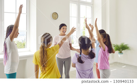 Happy sport trainer talking with her kids girls at the end of class standing in dance studio. Happy sport trainer talking with her kids girls at the end of class standing in dance studio. 130940133