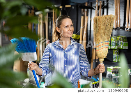 Casual woman holding two brooms while shopping in the supermarket Casual woman holding two brooms while shopping in the supermarket 130940698