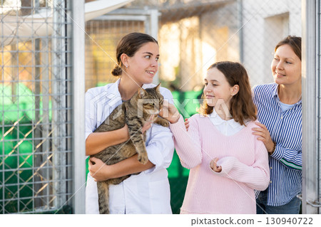 Female volunteer showing gray tabby cat to girl and mother in shelter 130940722