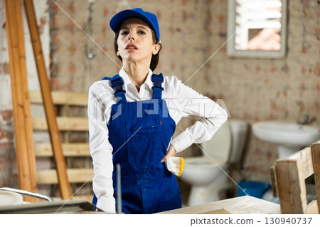 Portrait of confident female foreman in blue overalls in building under construction Portrait of confident female foreman in blue overalls in building under construction 130940737