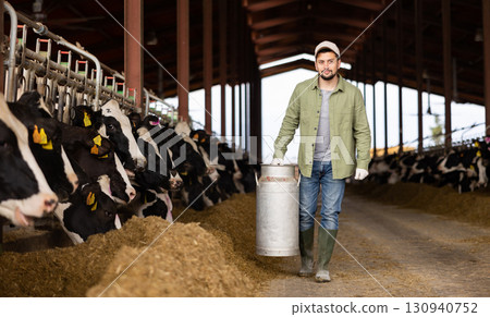 Farmer carrying milk churn near stall with cows in cowshed Farmer carrying milk churn near stall with cows in cowshed 130940752