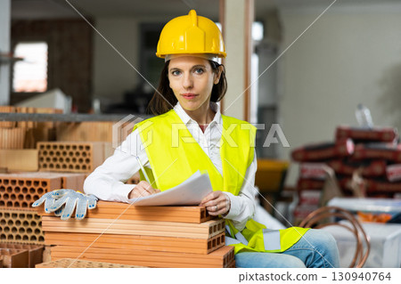 Female architect making list of tasks while supervising building under construction Female architect making list of tasks while supervising building under construction 130940764