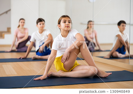Girl sitting in lord of the fishes pose during training with family Girl sitting in lord of the fishes pose during training with family 130940849