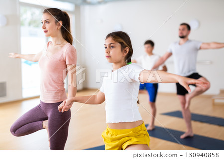 Young girl standing in tree pose with her mother during yoga training Young girl standing in tree pose with her mother during yoga training 130940858