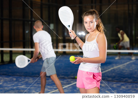 Portrait of happy woman with racket and ball in his hands on padel court 130940859
