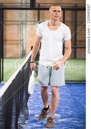 Padel player playing padel in a padel court indoor behind net 130940897