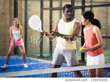 African American padel tennis trainer explaining forehand technique to woman 130940898