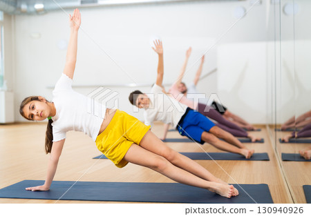 Preteen girl practicing Vasisthasana or Side Plank pose during family yoga workout Preteen girl practicing Vasisthasana or Side Plank pose during family yoga workout 130940926