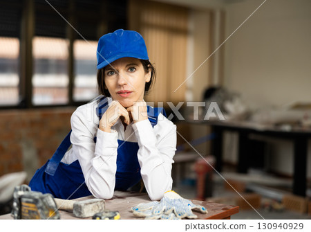 Positive woman repairer in uniform standing inside apartment and looking at camera 130940929