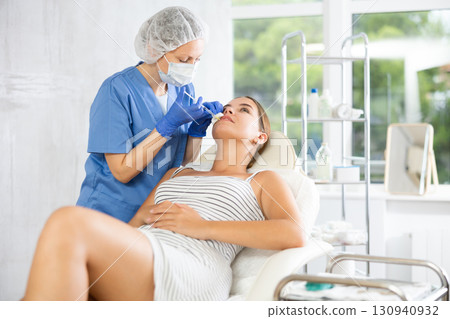 Adult woman cosmetologist makes injection in lips of patient 130940932