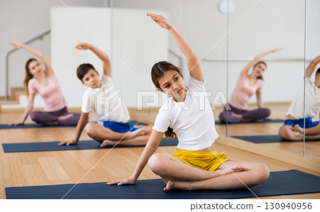 Girl doing stretching in Padmasana pose with brother and parents in yoga studio Girl doing stretching in Padmasana pose with brother and parents in yoga studio 130940956