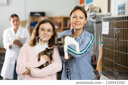 Preteen girl with mother standing in animal shelter holding cats 130941092