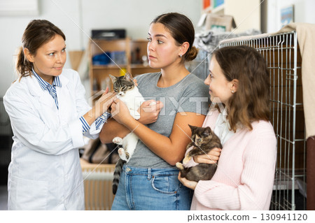 Female owner of animal shelter talking to girls adopting kitten 130941120