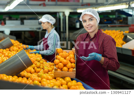 Cheerful girl worker with box of tangerines at fruit sorting factory 130941127