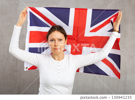 Sad young woman holding flag of Great Britain against unicoloured background Sad young woman holding flag of Great Britain against unicoloured background 130941235