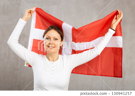Happy young woman holding flag of Denmark against unicoloured background Happy young woman holding flag of Denmark against unicoloured background 130941257