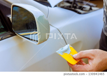 Car repair process with person applying filler to damaged side mirror at home garage Car repair process with person applying filler to damaged side mirror at home garage 130941465