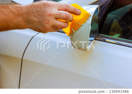 Man repairing car mirror using putty spatula in well lit garage setting Man repairing car mirror using putty spatula in well lit garage setting 130941466