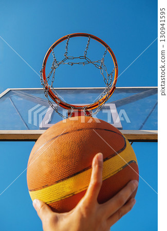 Hand holding basketball aiming for the hoop against clear blue sky. Sport and healthy lifestyle concept. 130941595