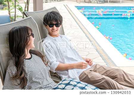 Couple sitting by the pool at a resort hotel on a trip Couple sitting by the pool at a resort hotel on a trip 130942033