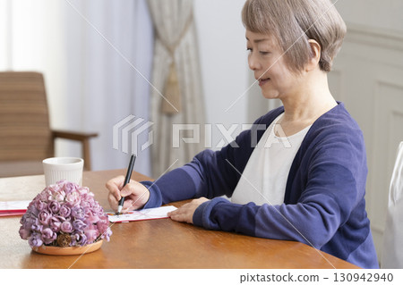 A senior woman writing the address on a gift envelope with a brush pen A senior woman writing the address on a gift envelope with a brush pen 130942940
